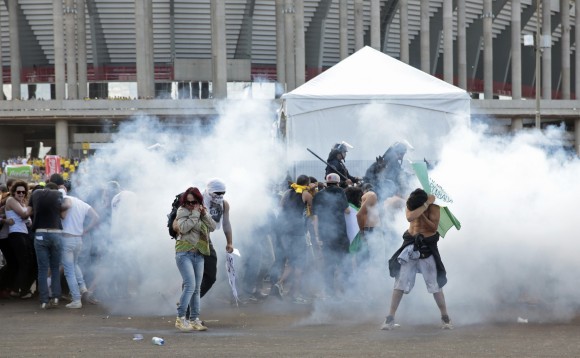 Activists and students stand in a cloud of tear gas as they clash with riot police outside the Mane Garrincha National Stadium in Brasilia